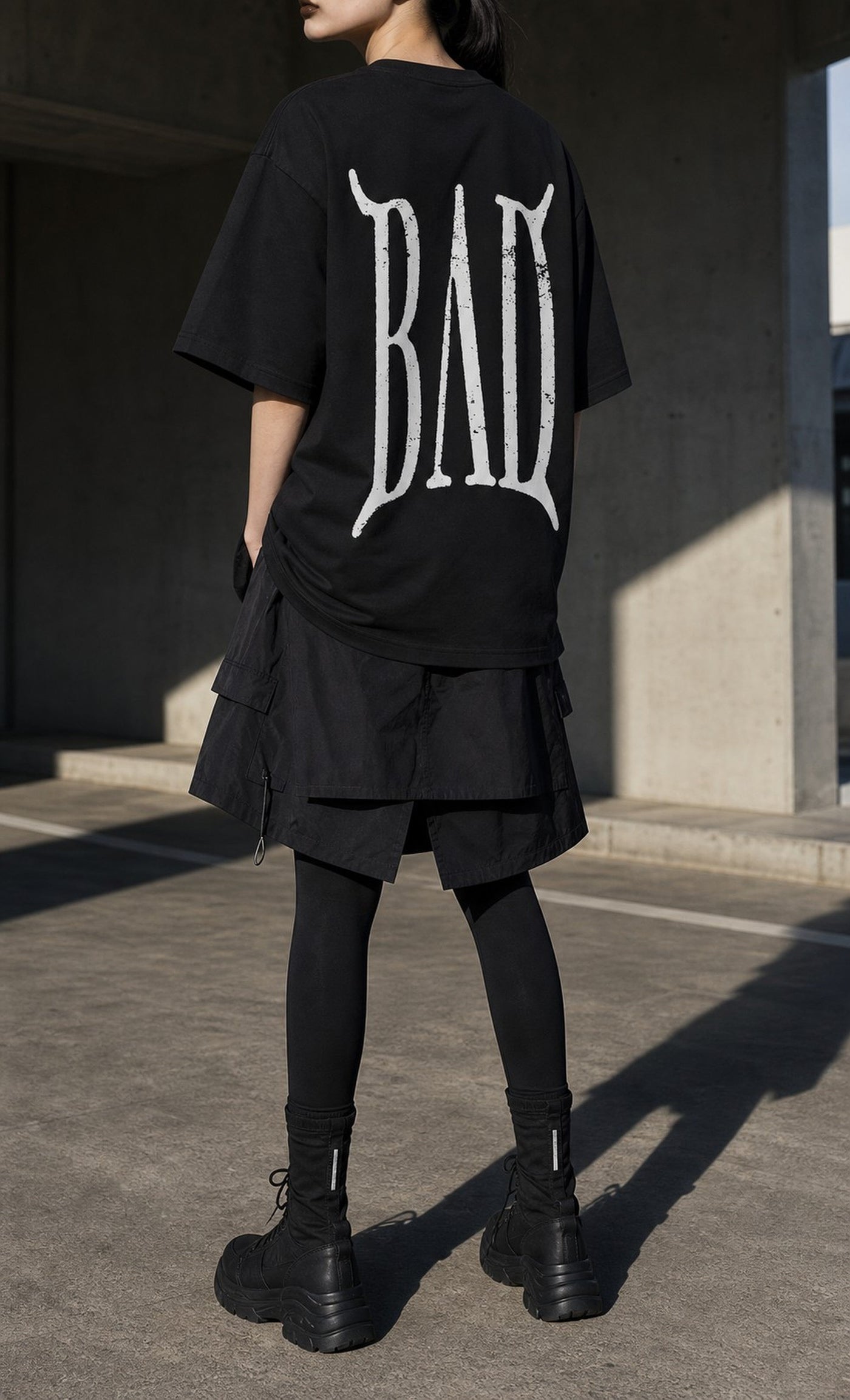 BAD Tee worn from behind against raw concrete in hard daylight